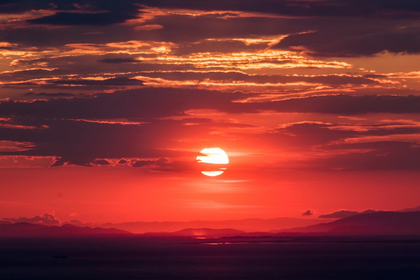 A crimson sunset over the sea and distant hills